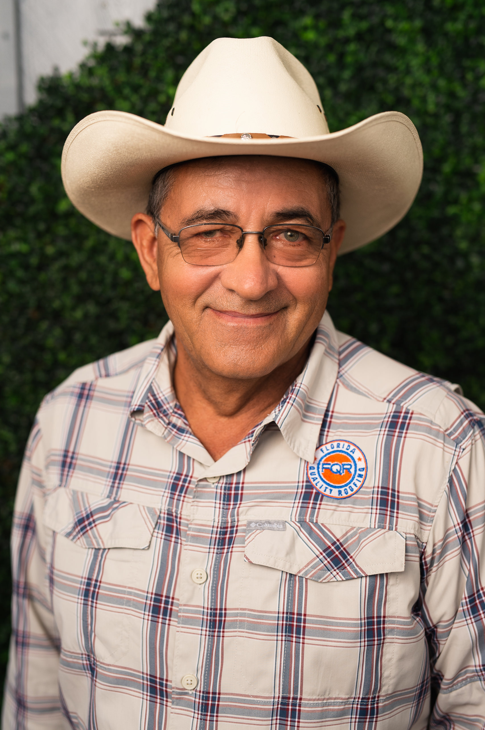 Florida Quality Roofing Headshot of man wearing cowboy hat and glasses in a mostly white shirt with FQR logo