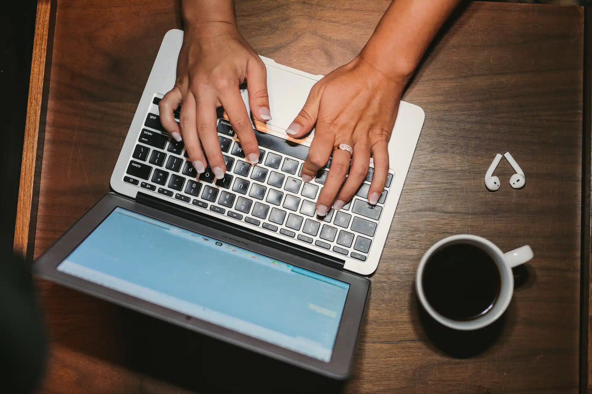 Overhead view of woman using a desktop on a table with earbuds and a cup of coffee nearby