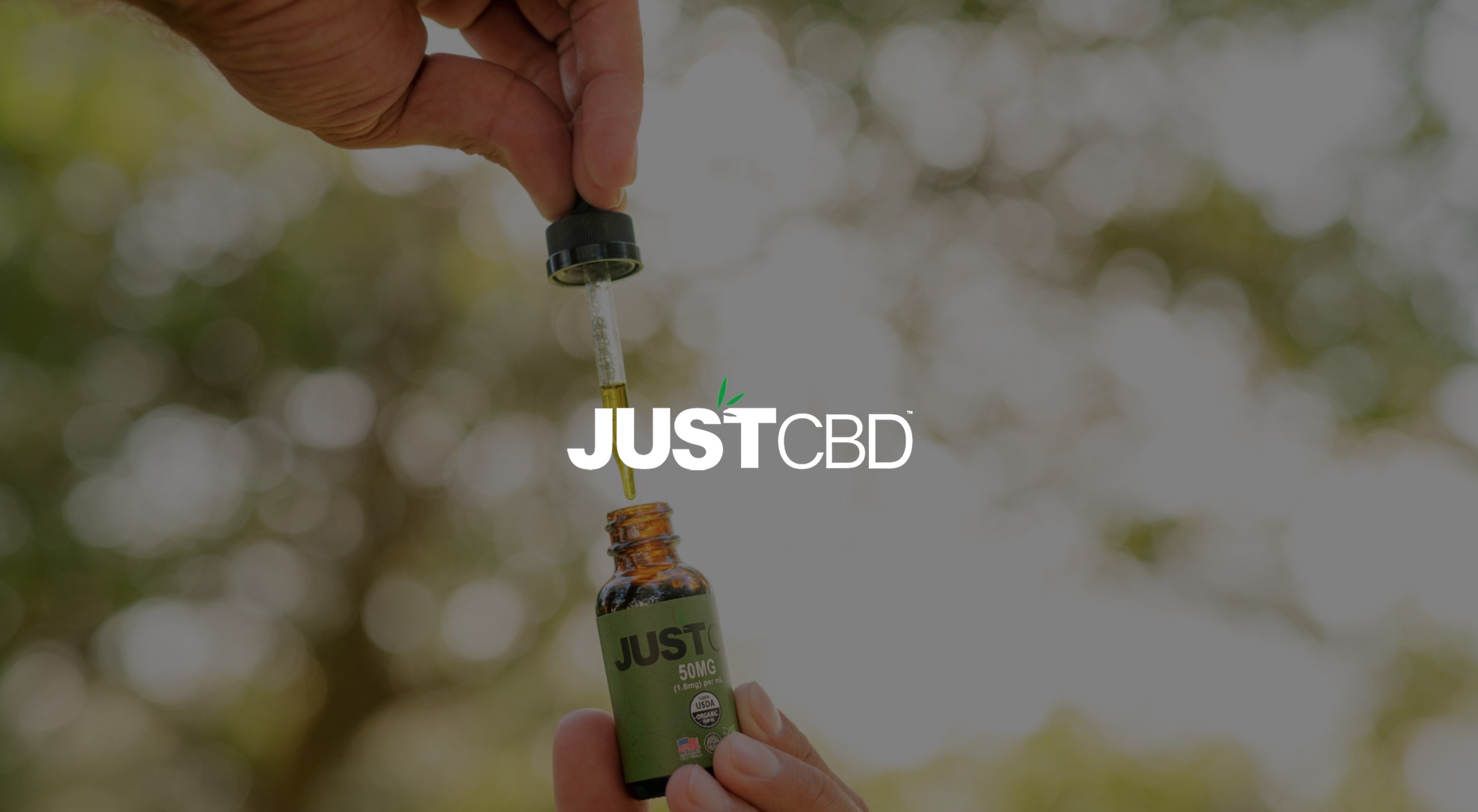 White JustCBD logo Photo Services with dimmed background of person using dropper in bottle