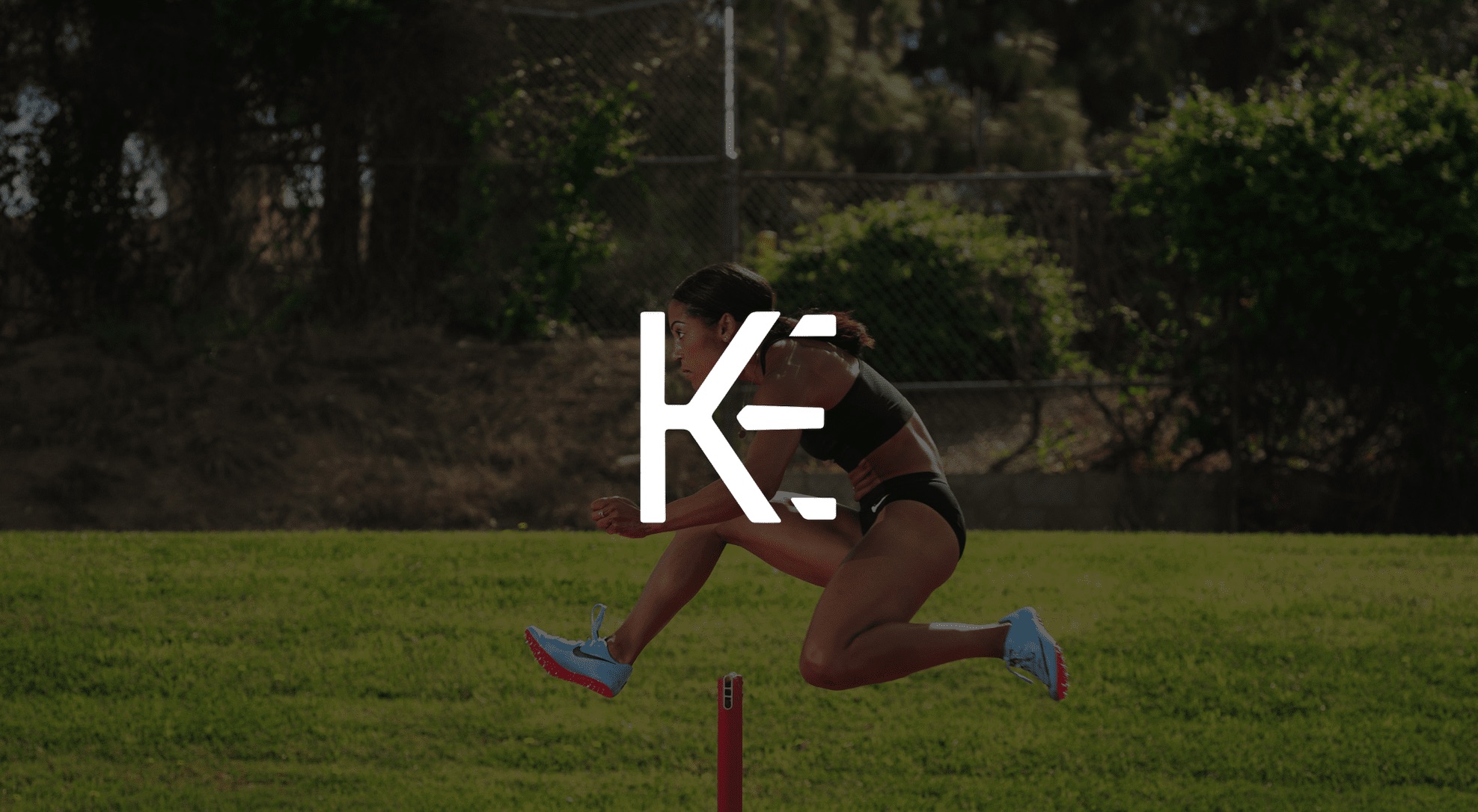 Professional Photography Services by C&I Studios White KE logo against a dimmed background side view of a female track athlete jumping a hurdle