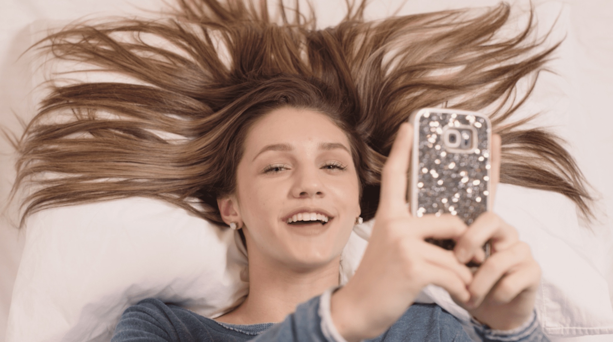 Hawthorne Suites by Wyndham Woman with long brown hair splayed on a pillow doing a selfie