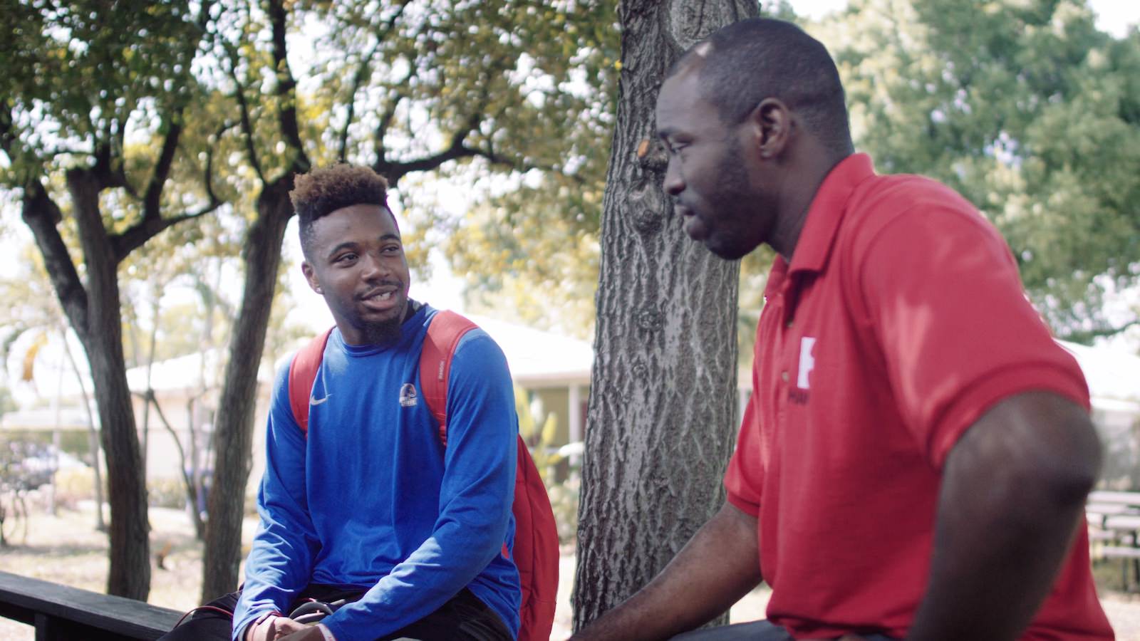 IU Professional marketing for nonprofit organizations Teacher wearing a red shirt talking to a student wearing a blue long sleeved shirt and red backpack outside