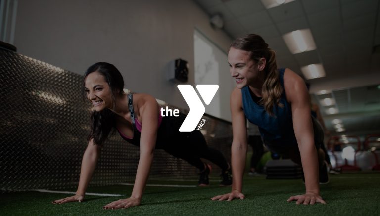 YMCA Two woman doing planks on the green turf in a gym