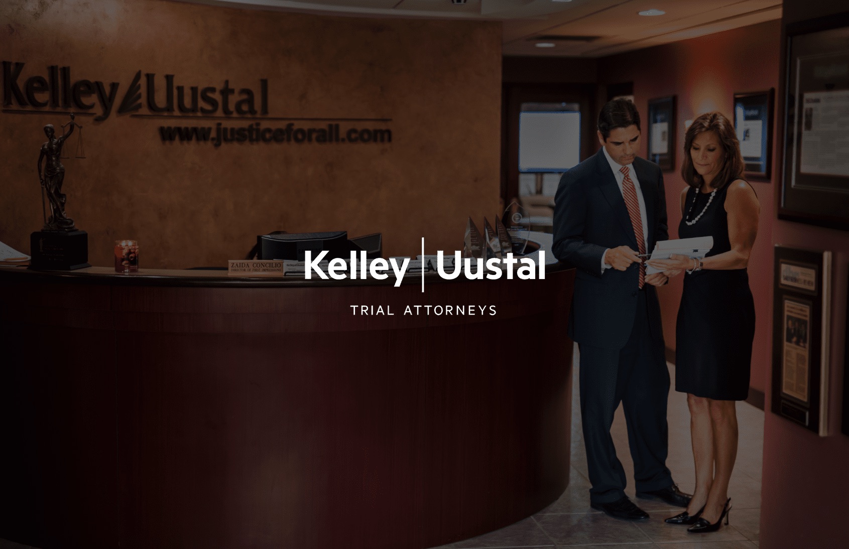 Kelley & Uustal Trial Attorneys logo with a male and female attorney going over a case in a lobby in the background
