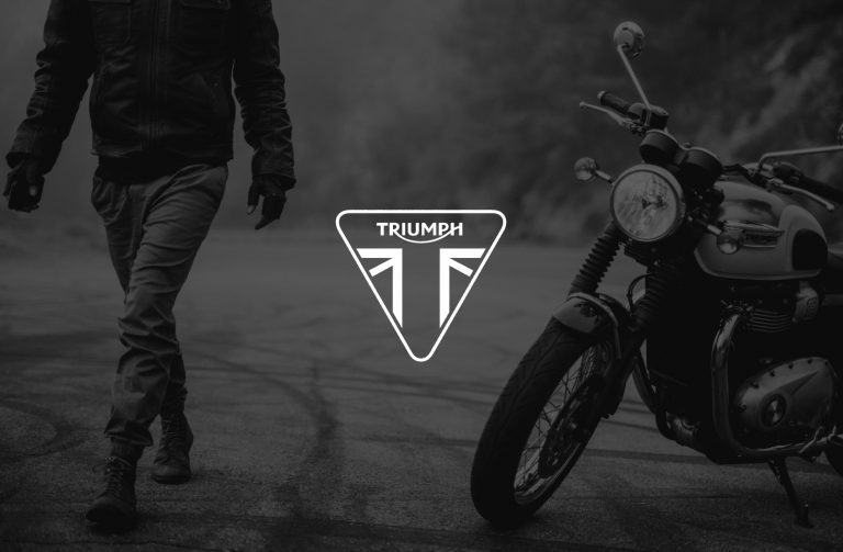 IU C&I Studios Page White Triumph logo with black and white photo of the rider walking away from the Bonneville T100 in the background