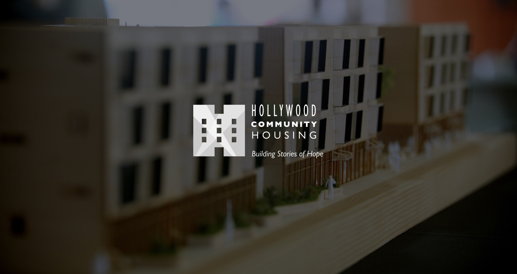 White Hollywood Community Housing Building Stories of Hope with dimmed background showing closeup of scale model of buildings on piece of wood