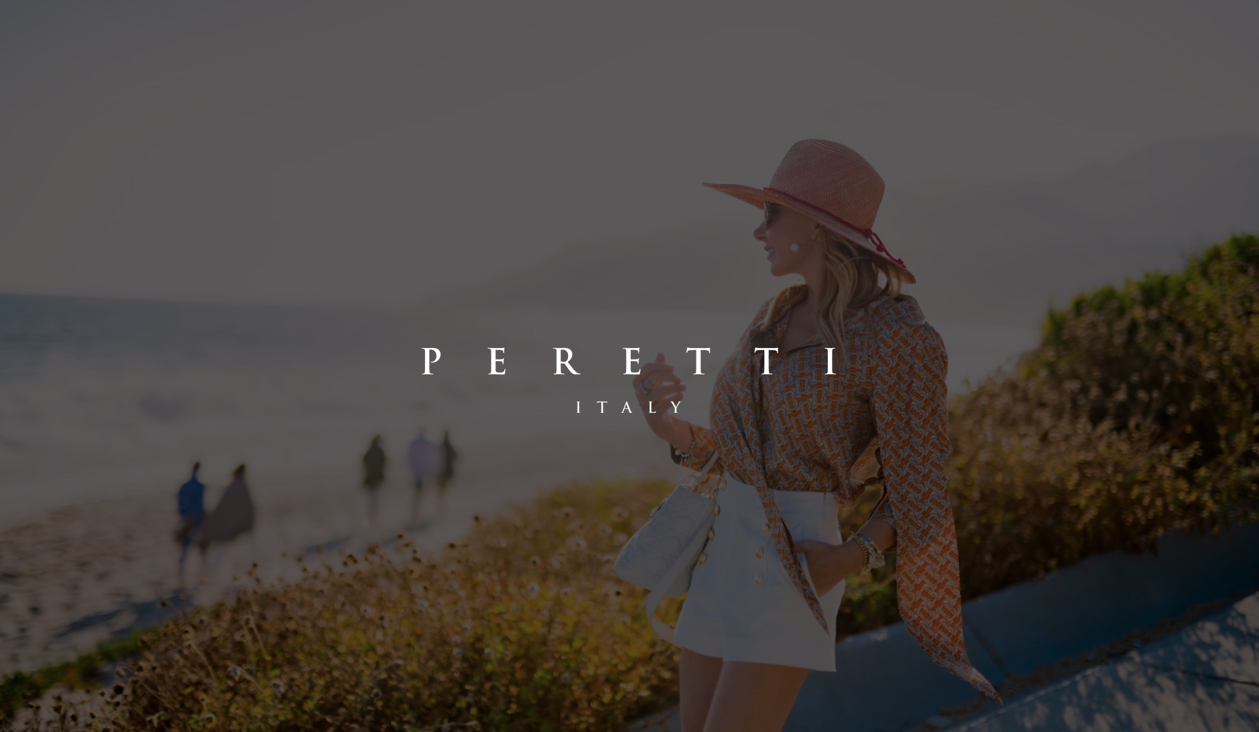 IU C&I Studios Page White Peretti Italy title with dimmed background side profile of woman wearing short white skirt, patterned top, red hat and shades standing by the beach
