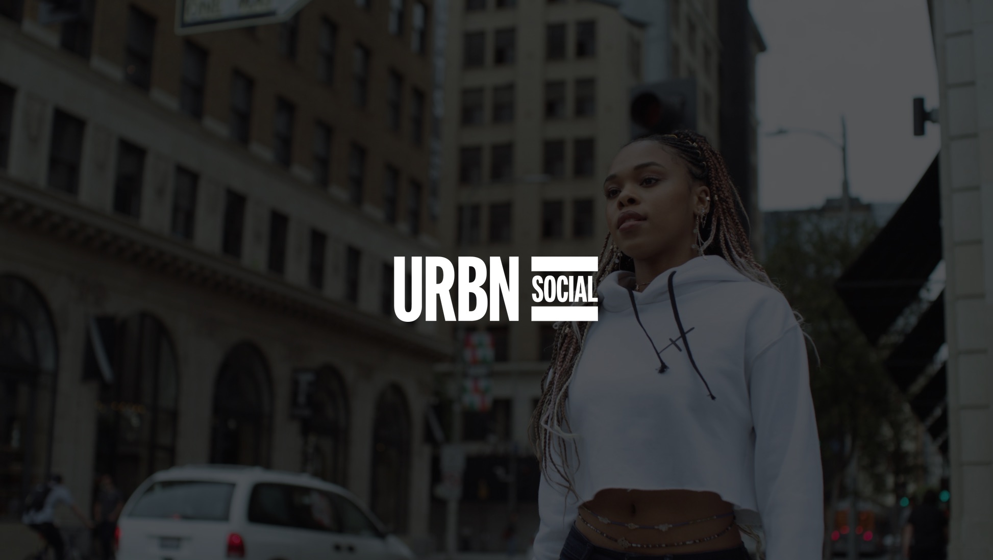 White URBN Social logo on dimmed background of woman wearing a white Uncreative sweatshirt top looking off to the side
