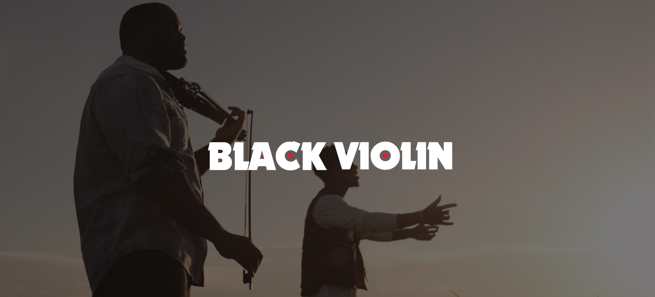 Red and white Black Violin logo on background closeup side profile of man playing violin with another man singing next to him