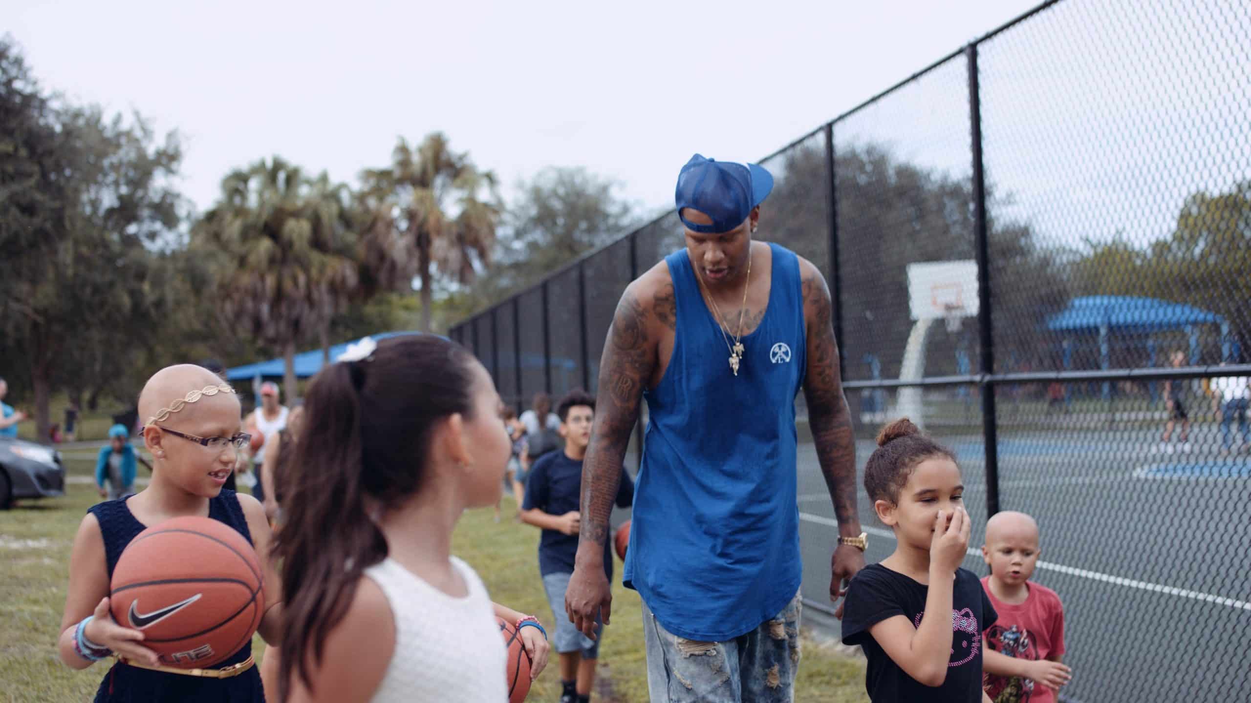 Charlie V What is Alopecia? Charlie V wearing blue shirt and jean shorts walking with children next to a basketball court