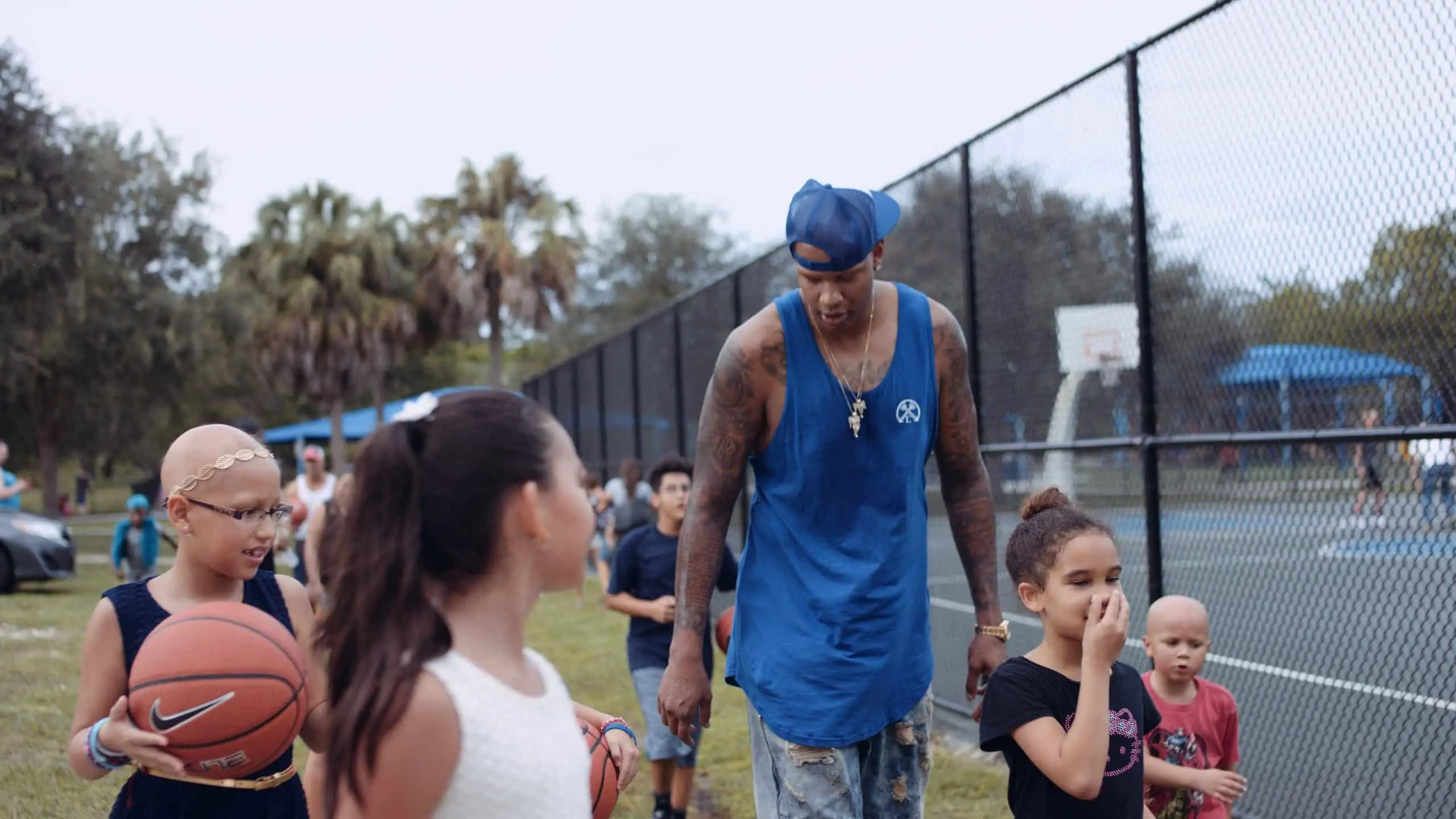 cis-page-what-is-alopecia Charlie V wearing blue shirt and jean shorts walking with children next to a basketball court