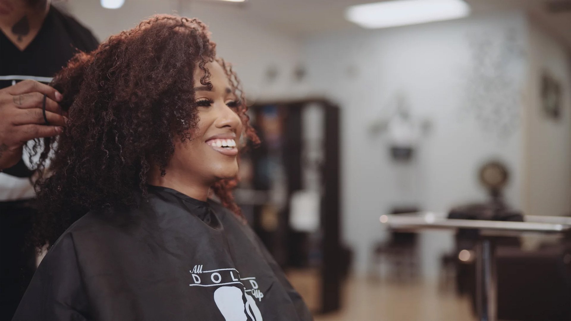 8K All Dolled Up Month 1 Side profile of woman with brown fizzy hair smiling at a hairdresser with a male hairdresser standing behind her