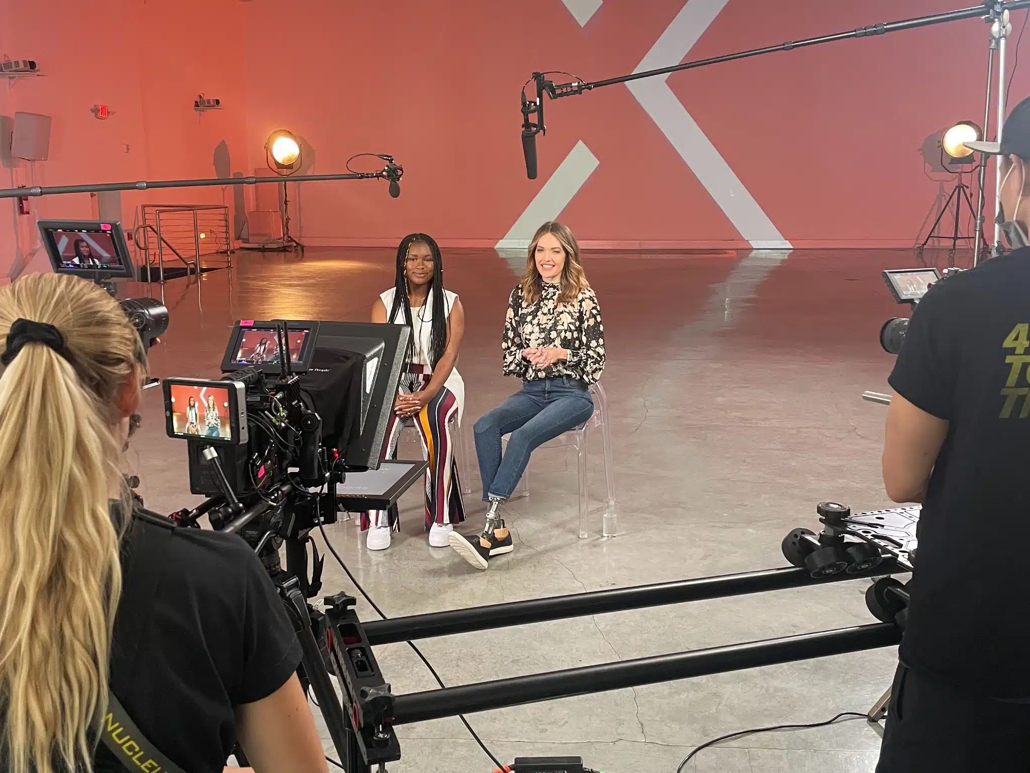 Two women on a set smiling being filmed by two crew members