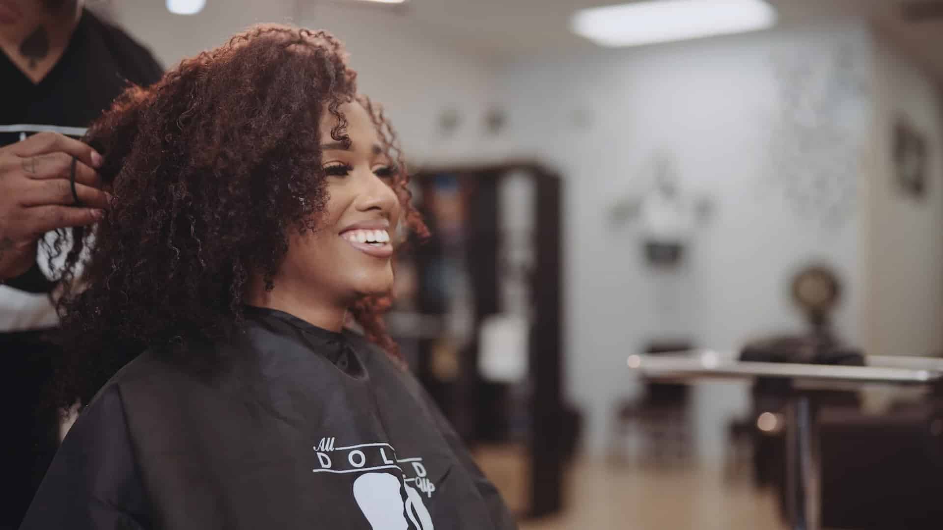 All Dolled Up Month 1 8K All Dolled Up Month 1 Side profile of woman with brown fizzy hair smiling at a hairdresser with a male hairdresser standing behind her