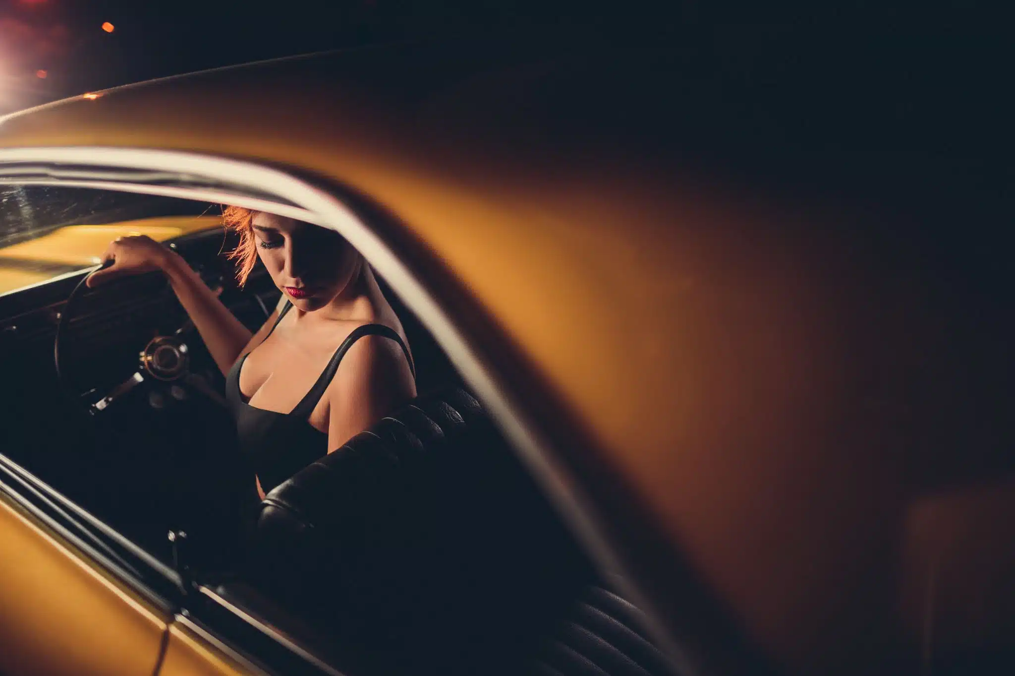 View from behind of woman in an orange vintage car with black seats looking back over her seat looking down