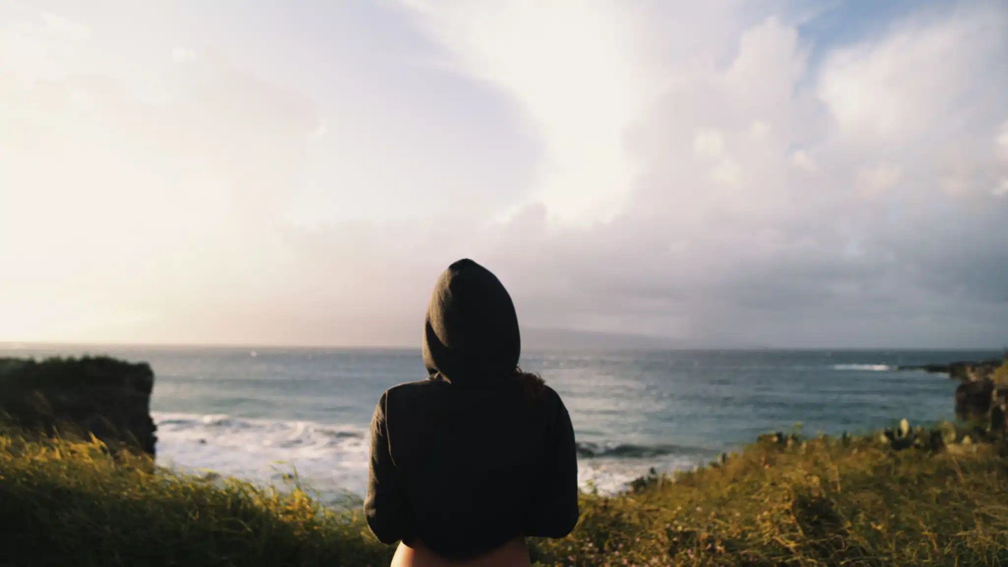 Shooting on Location vs. Shooting in a Studio Rental and When You Need to Use Both View from behind of woman wearing a hoodie looking out at the water from a ciff