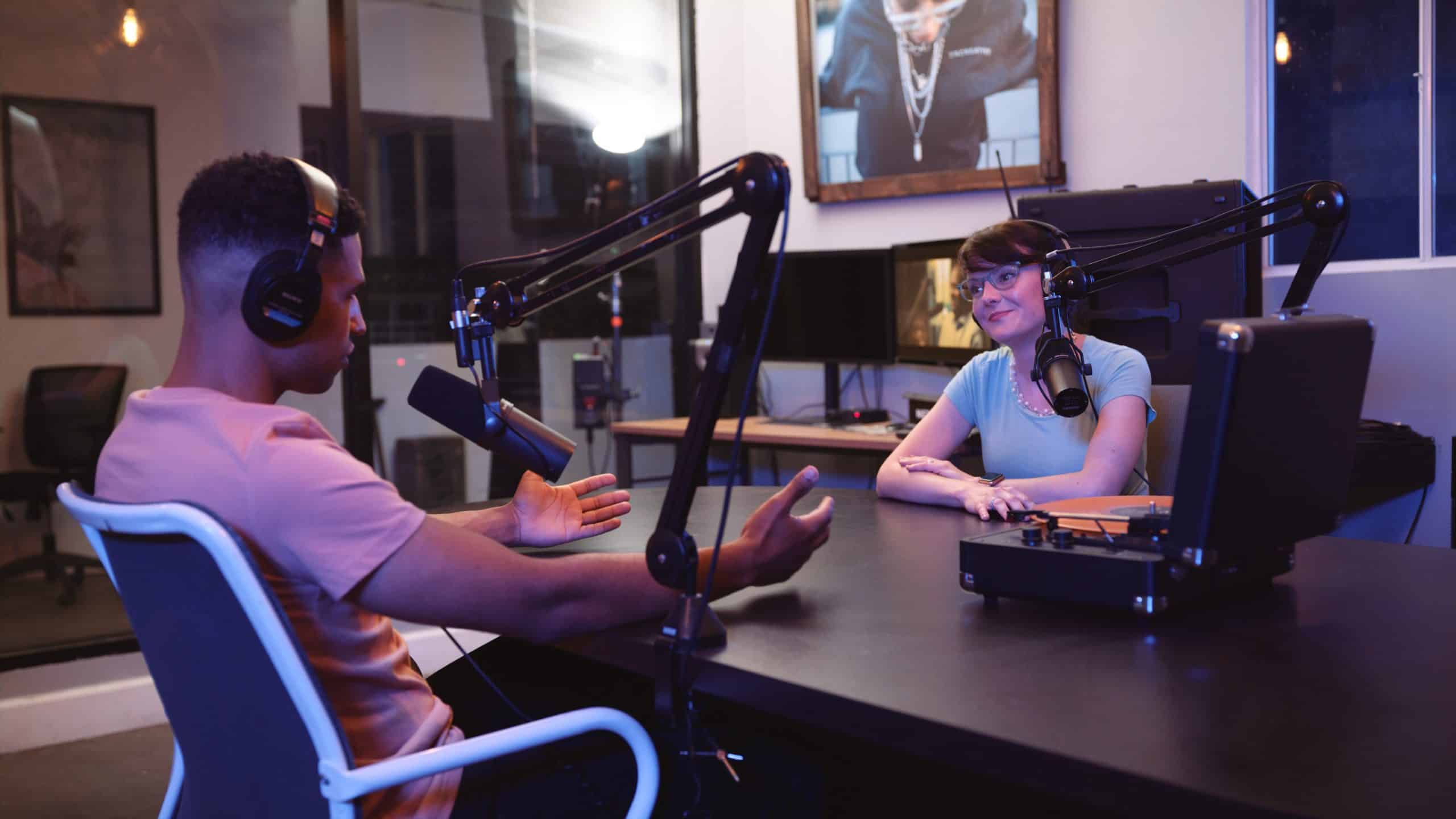Podcast Rental Shoot LA Studio with audio and video equipment and gear Side profile of a man wearing black headphones and a peach colored t shirt with a woman by microphones