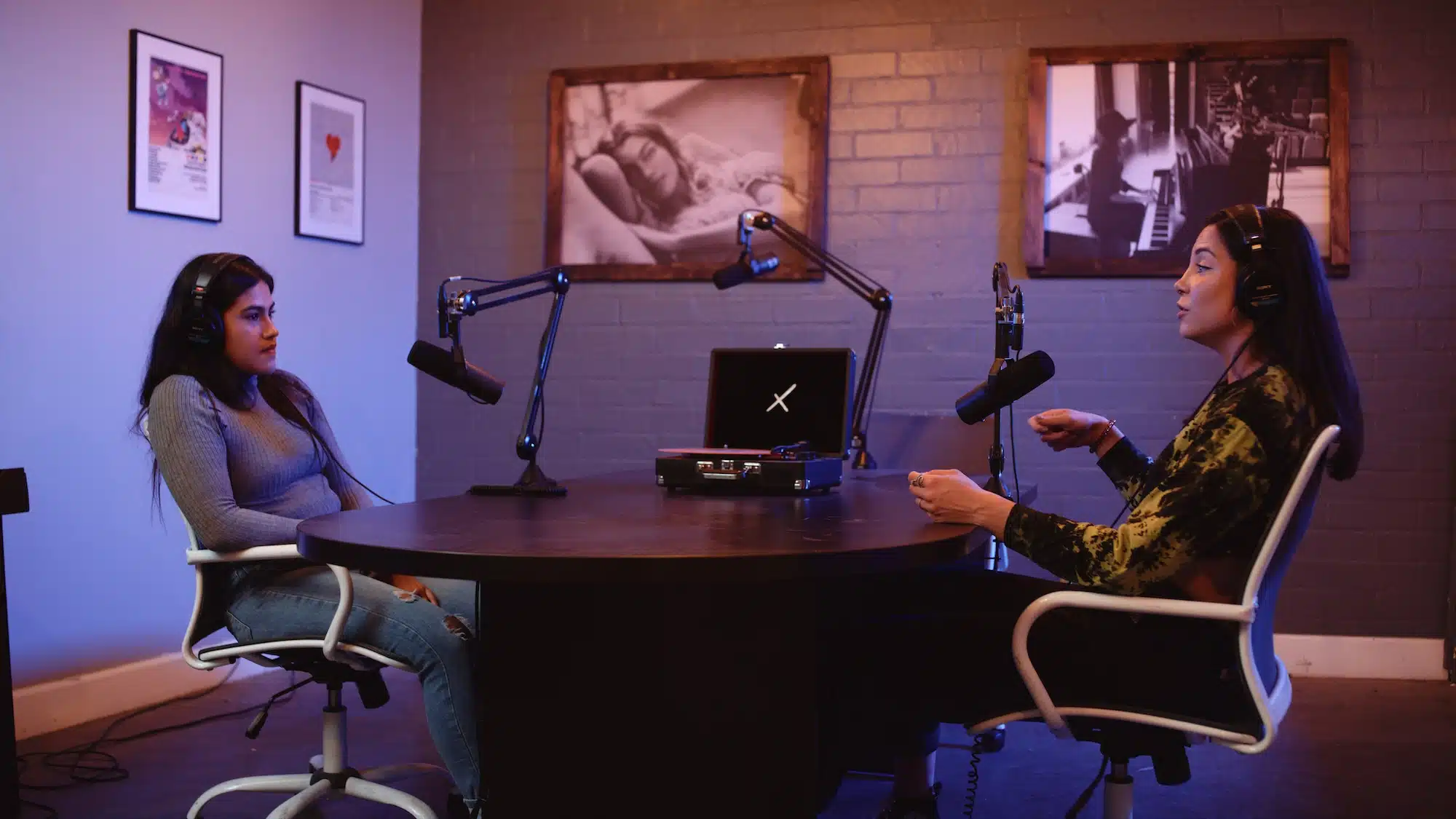 Two women both wearing black headphones by microphones doing a radio show with vinyl turntable in the background