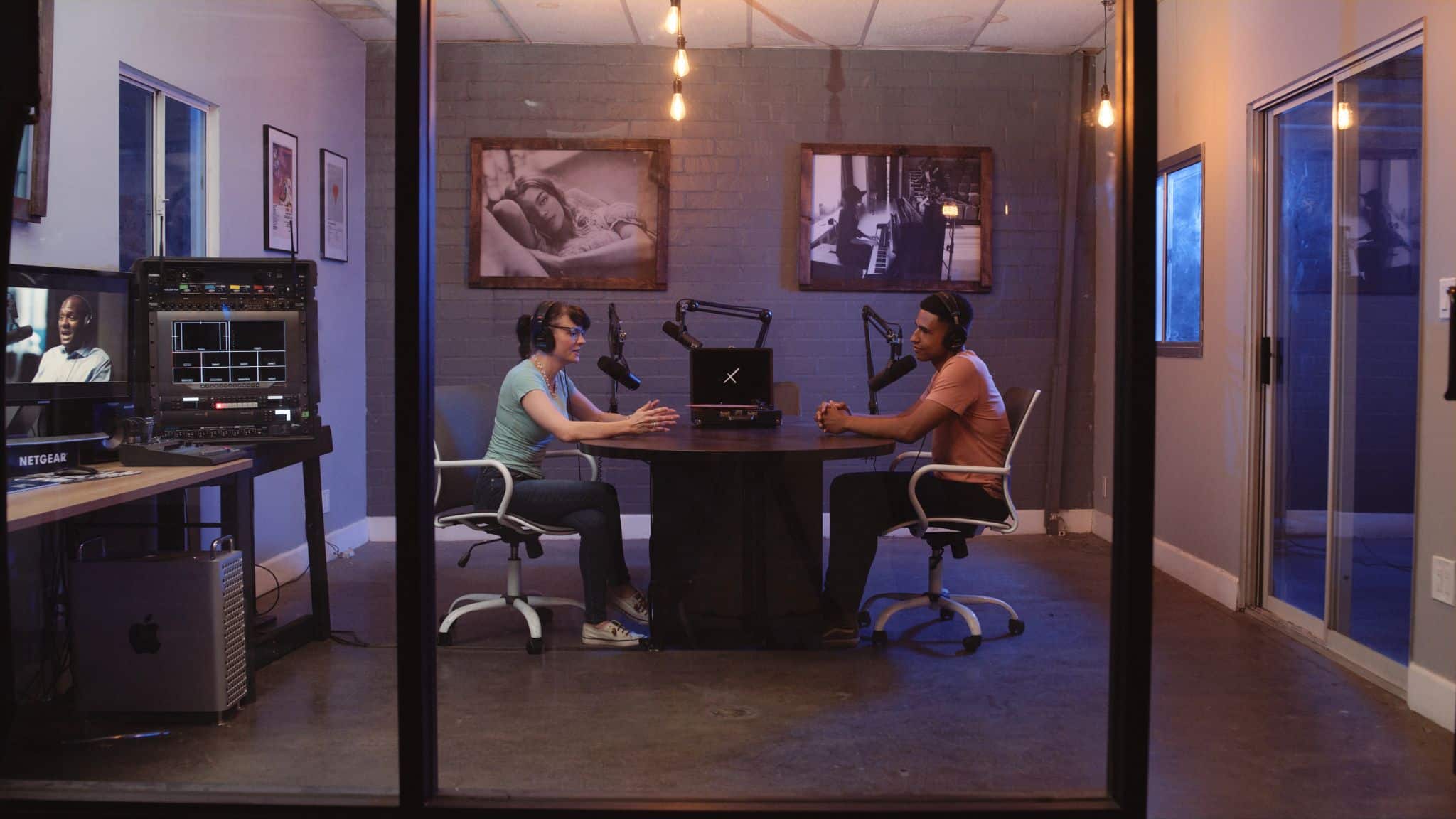 Side profile of man and woman doing a radio show in a room with a vinyl turntable in the background