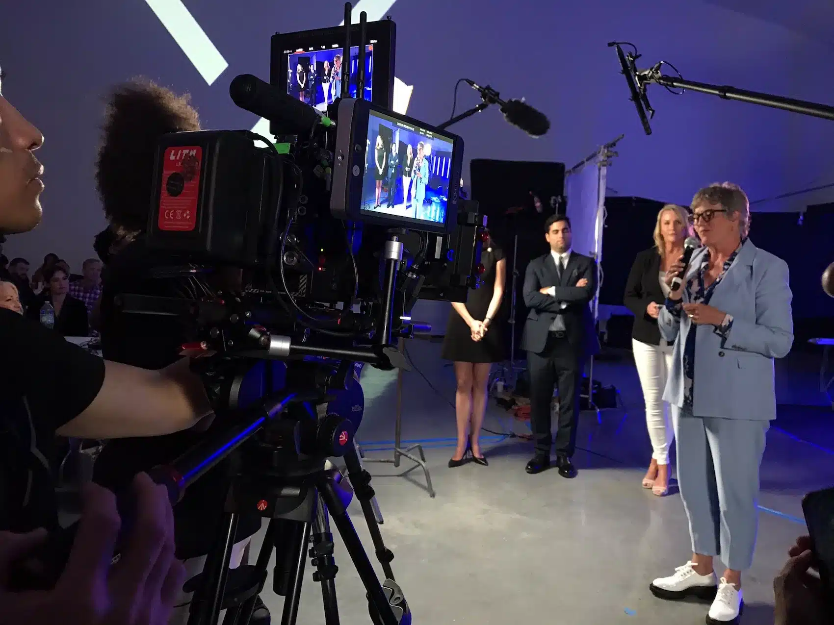 Hire Full Crew Closeup of male crew member filming a woman wearing a light blue dress suit talking