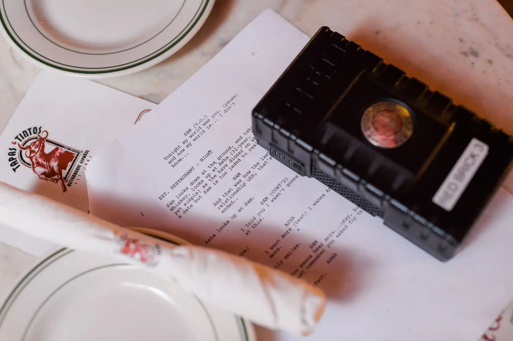 Tips from Film Professionals on Pre Producing a Documentary Closeup of Red Brick on script by a white plate and silverware wrapped in a napkin