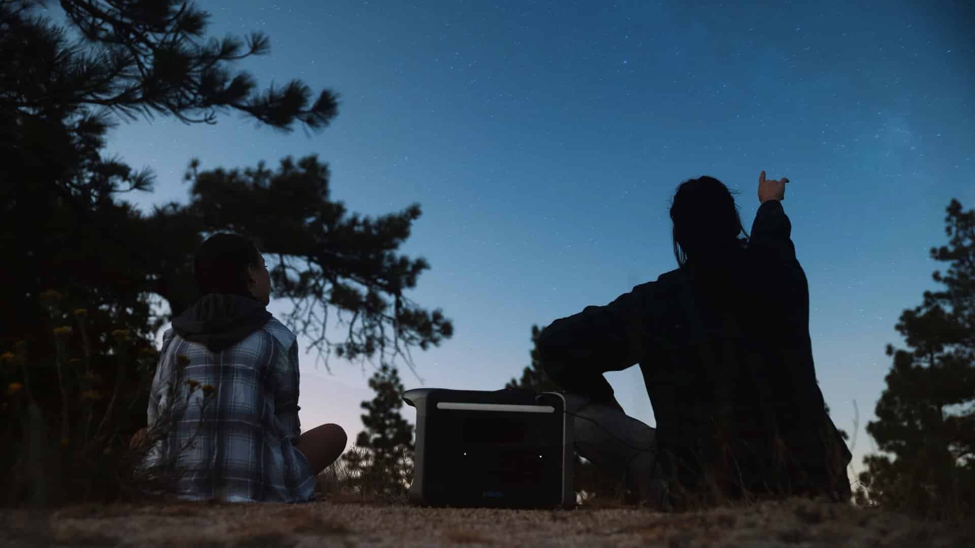 View from behind of two people looking up at the night sky with one pointing to the sky