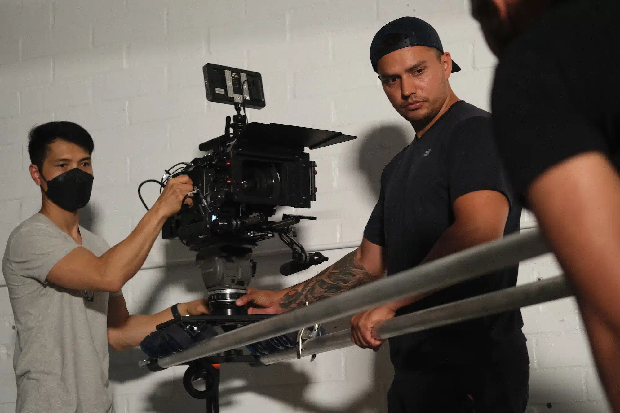 Two male crew members using a video camera with one wearing a black mask