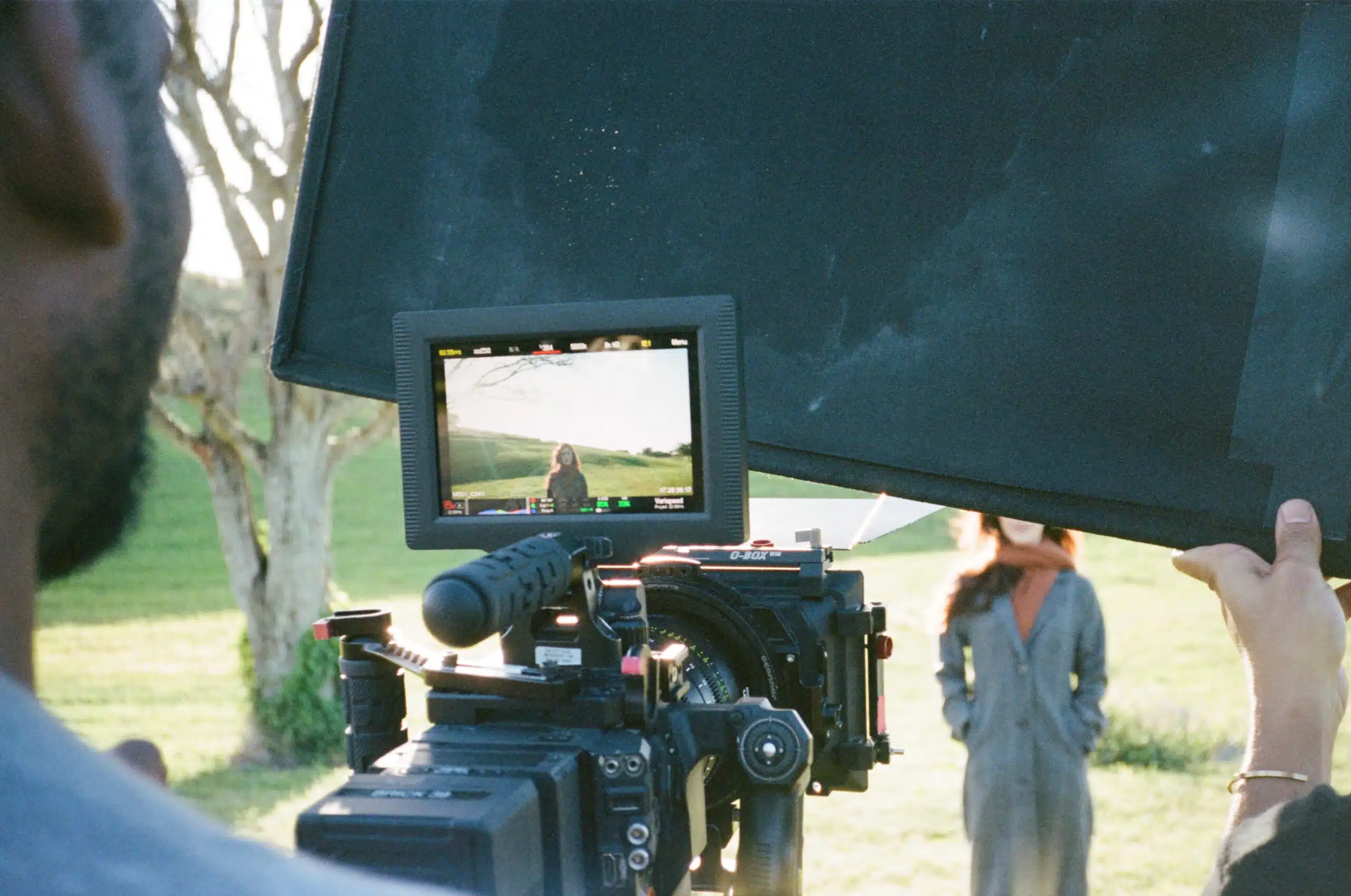 Things that most people forget when producing a video shoot Joshua using video camera on a woman standing in a field while another crew member holds a black screen