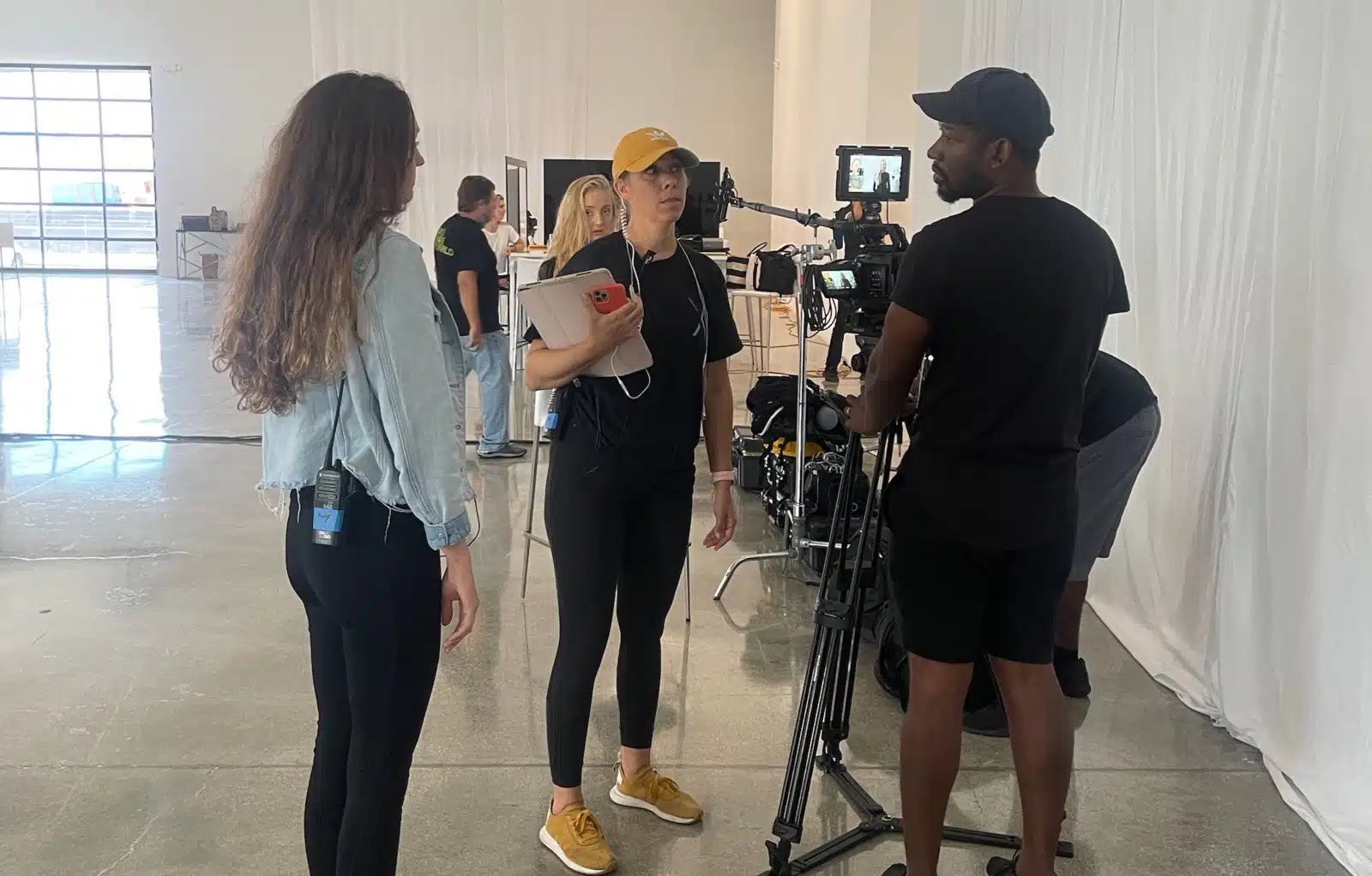 What Makes a Good PA View from behind of Joshua on set wearing a black cap by a video camera talking with two female crew members