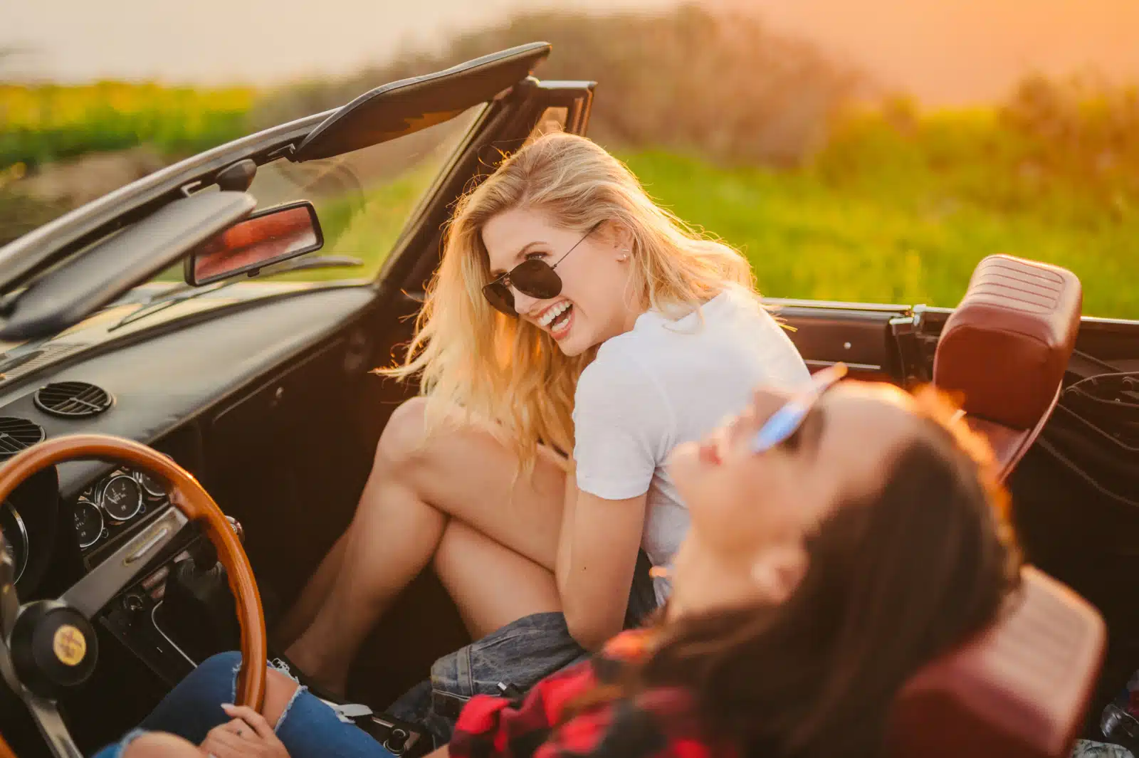 Side profile of two women sitting in a vintage car laughing