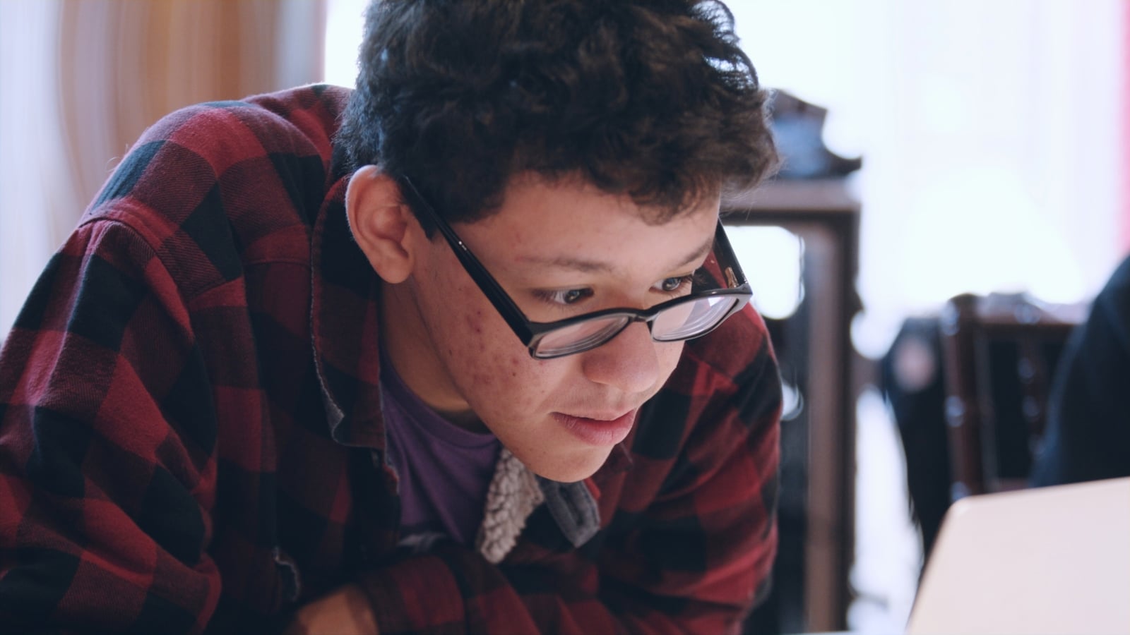 Headshot of young man wearing glasses as well as red and black flannel jacket