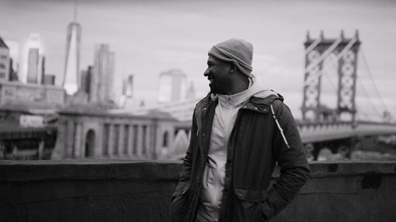 Black and white of Joshua Miller smiling looking away from the camera at the city from a rooftop