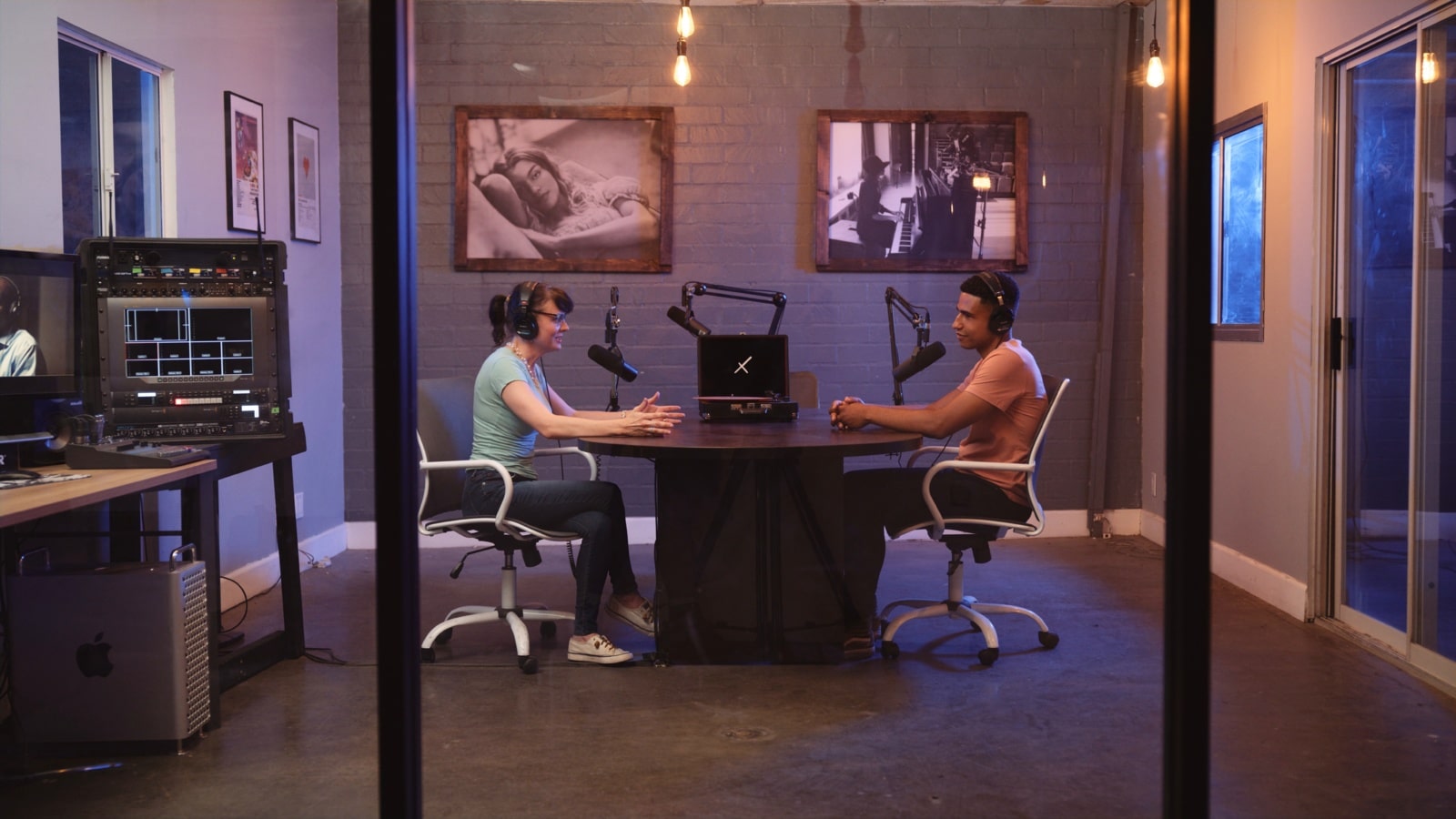 Side profile of woman ding a radio show with man in a room with microphones and an old vinyl turntable