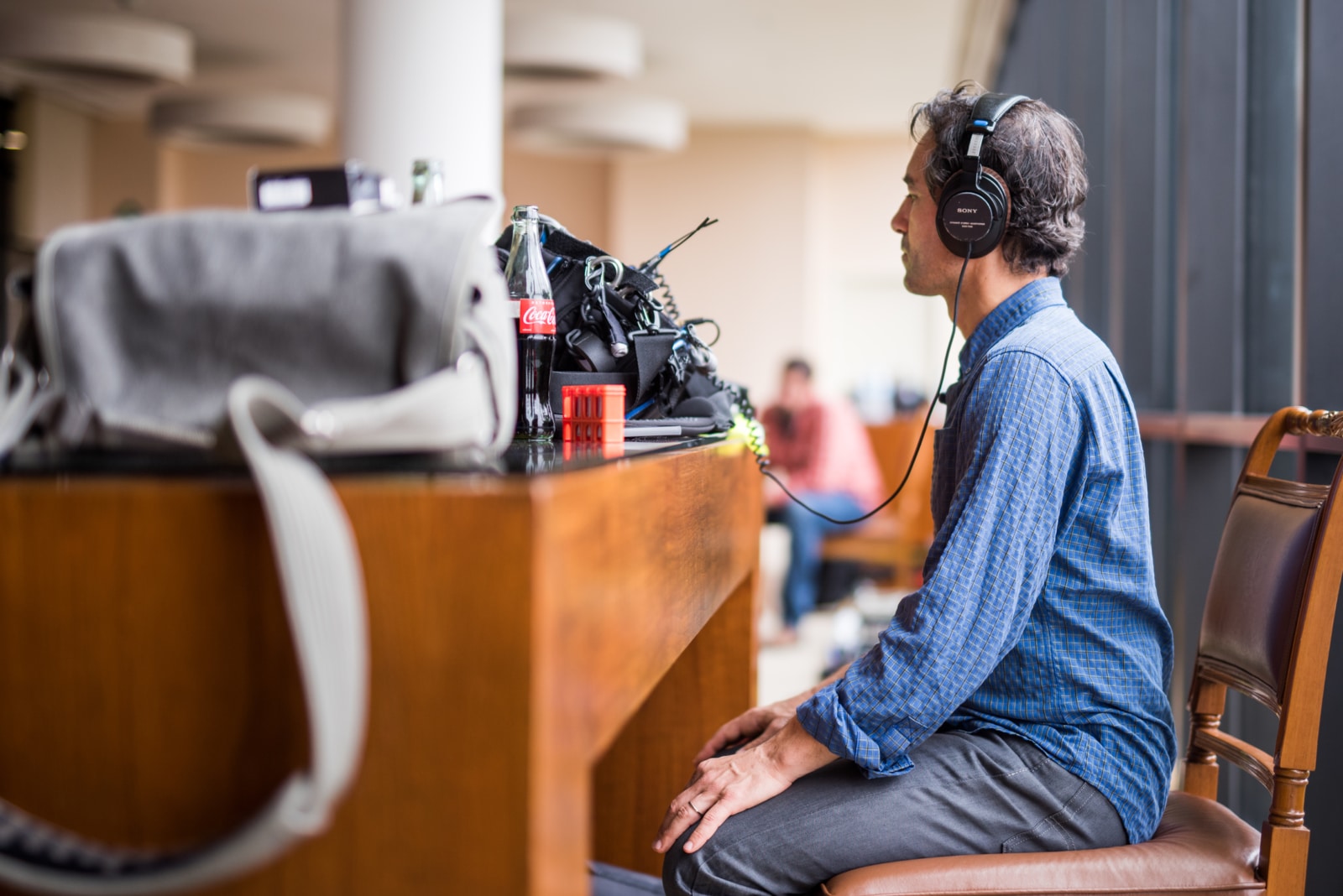 Side profile of a man wearing a blue shirt and gray pants as well as headphones listening to audio by a table