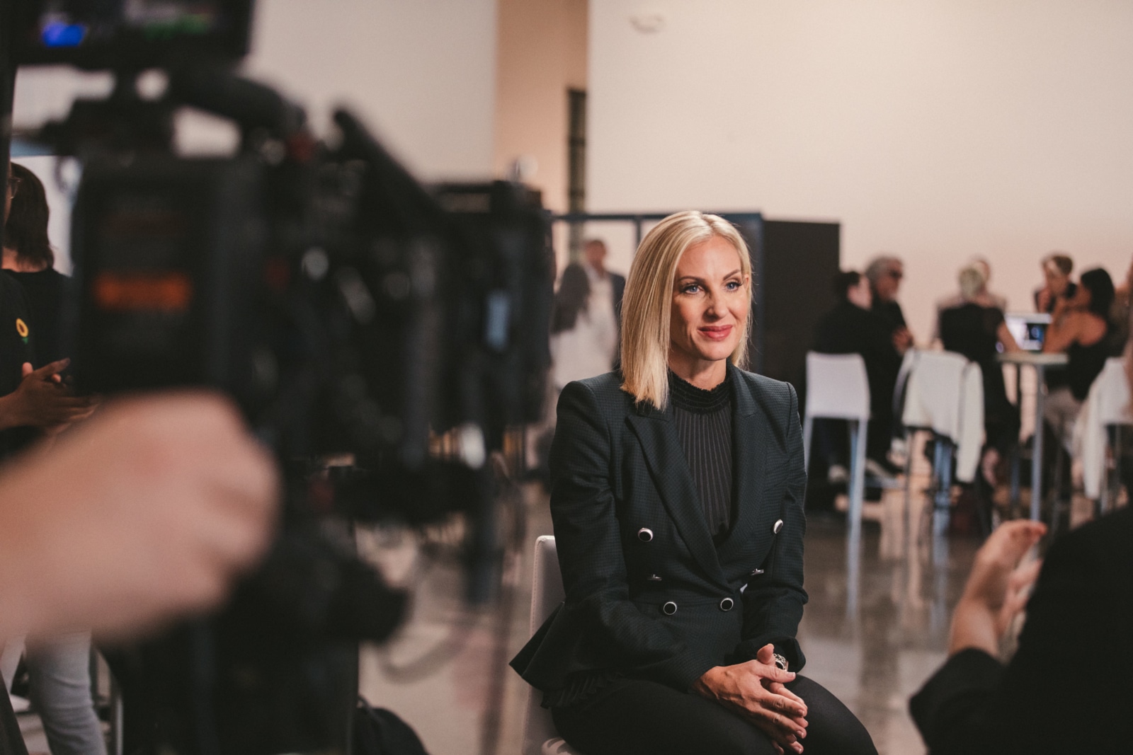 Woman with short blond hair posing for the camera sitting on a chair wearing a black dress suit