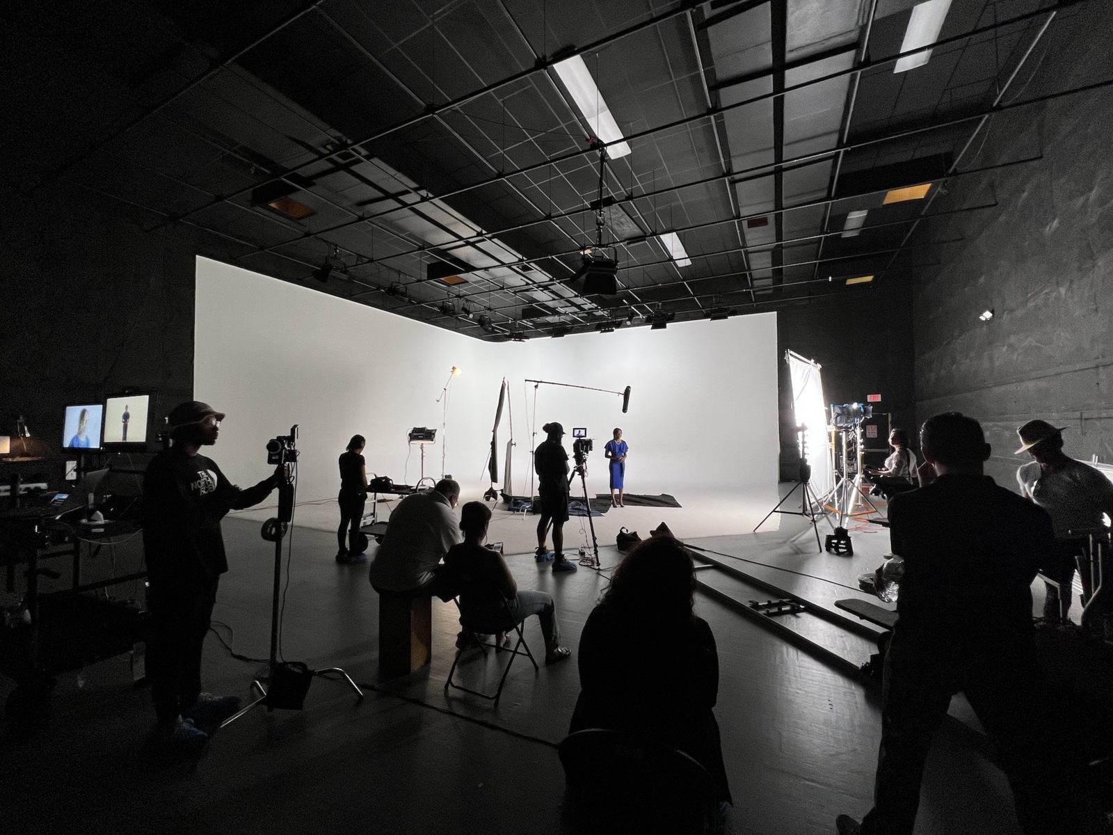 IU C&I Studios Page and Post Outsourcing Video Production Numerous crew members working on set while a woman wearing a blue dress is waiting against a white backdrop