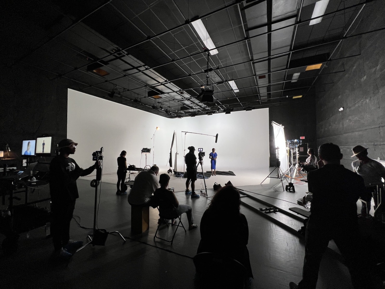 Outsourcing Video Production Numerous crew members working on set while a woman wearing a blue dress is waiting against a white backdrop
