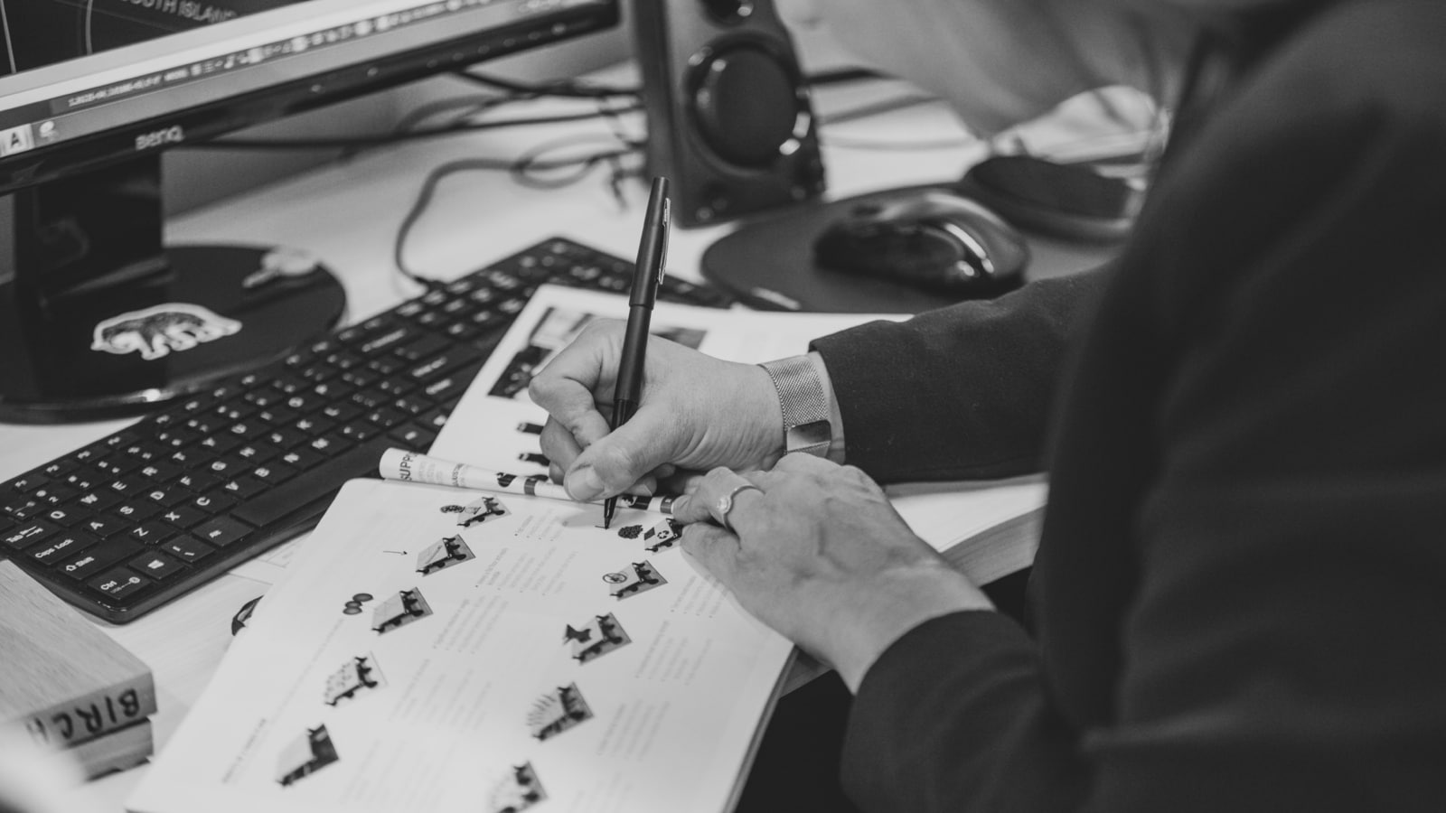 Black and white side profile of person writing in a book with desktop monitor and mouse nearby. Corporate Video Production