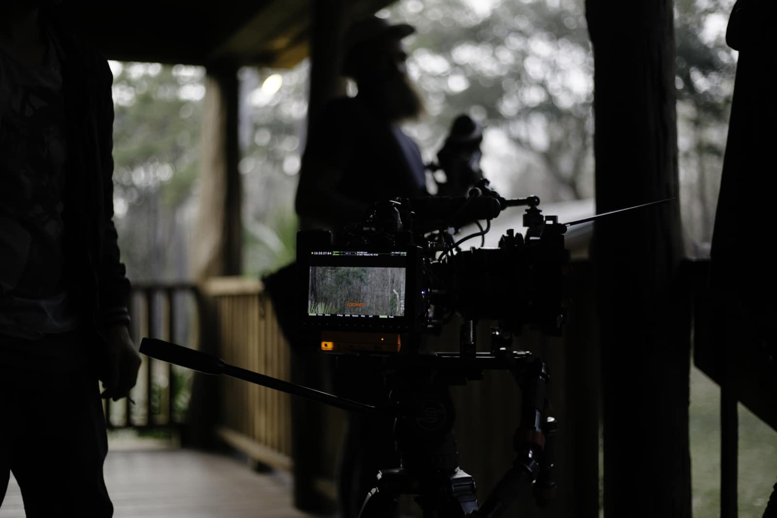 Closeup of video camera with crew members standing around on a porch