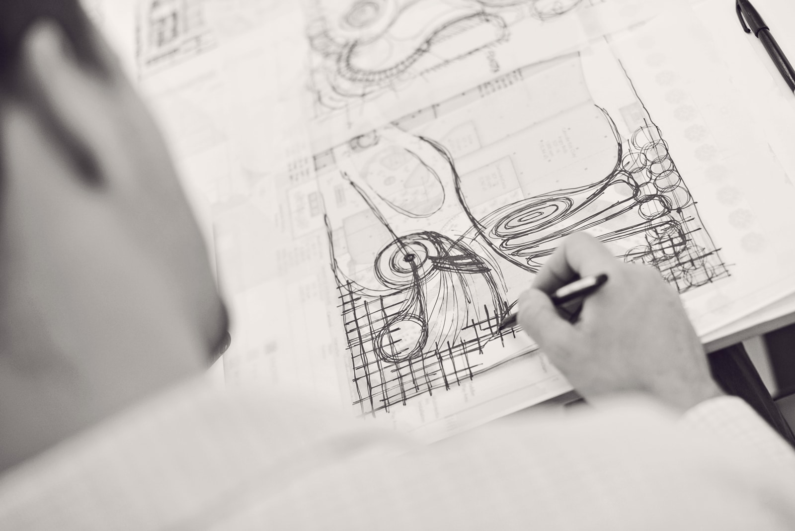 View over shoulder of man using a pen and drawing on a piece of paper