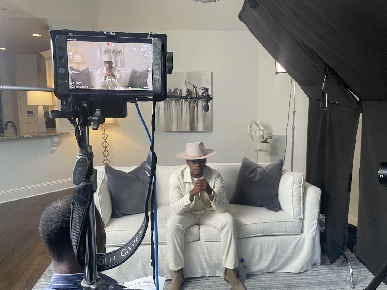 On set with Neyo in a white suit sitting on a white sofa with closeup of video monitor in the foreground