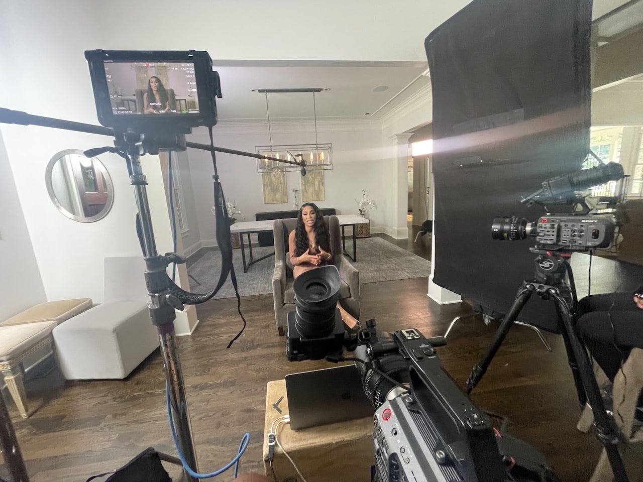 Tamar Braxton with long brown hair sitting on a gray chair talking with equipment around