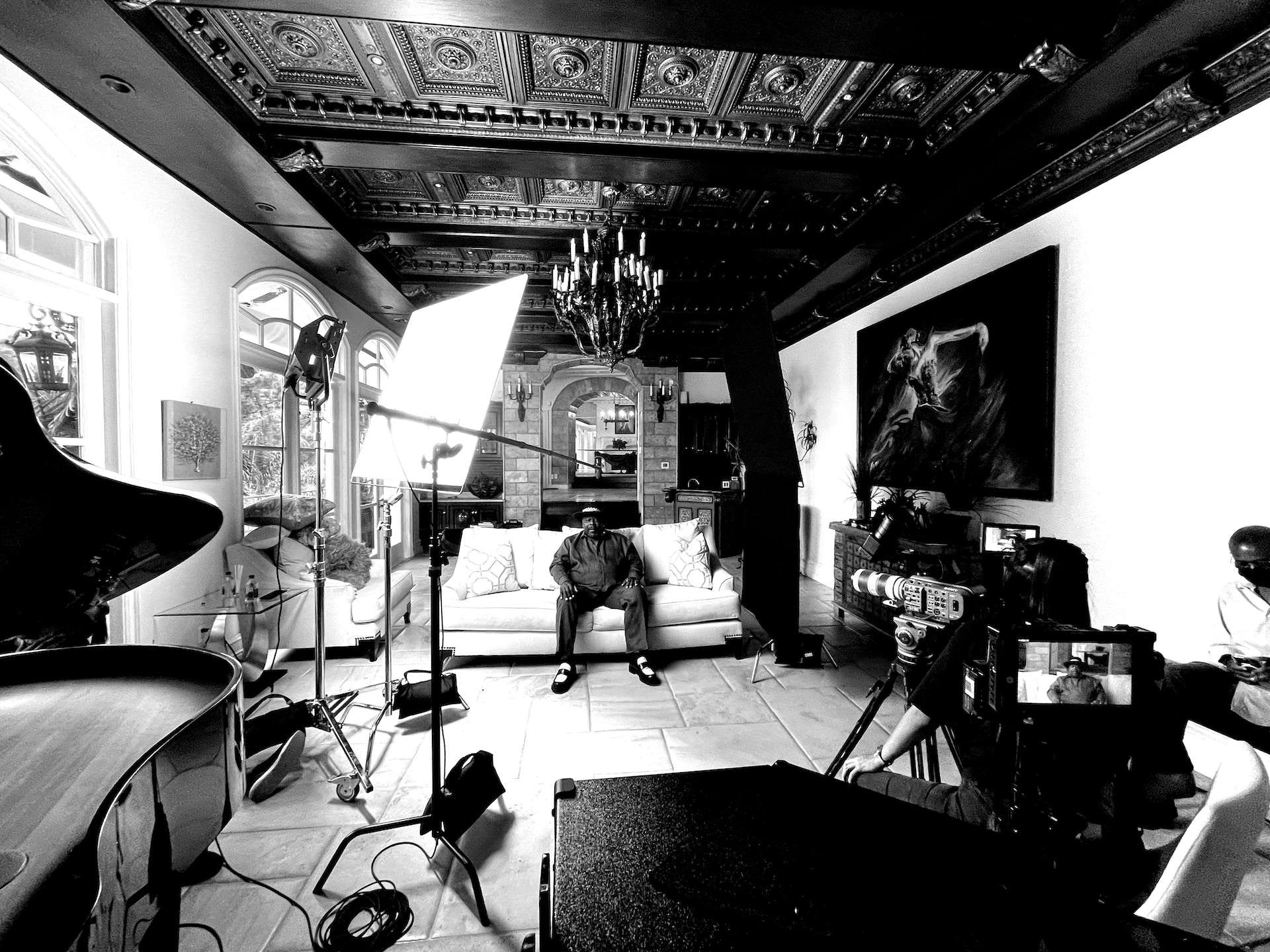 Cedric The Entertainer sitting on a set surrounded by crew and equipment black and white