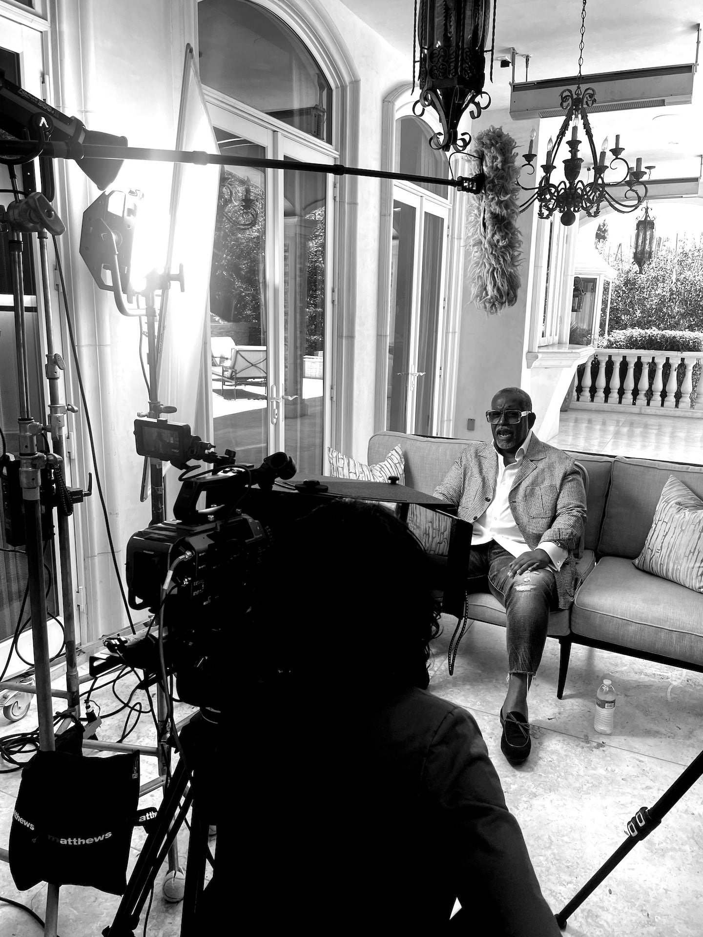 Dr. Todd Boyd sitting on a set surrounded by equipment and a female crew member filming black and white