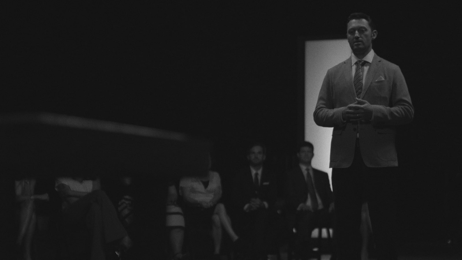 Reality TV Show Formats From Competition to Docuseries Black and white of man standing and a group of people behind him sitting