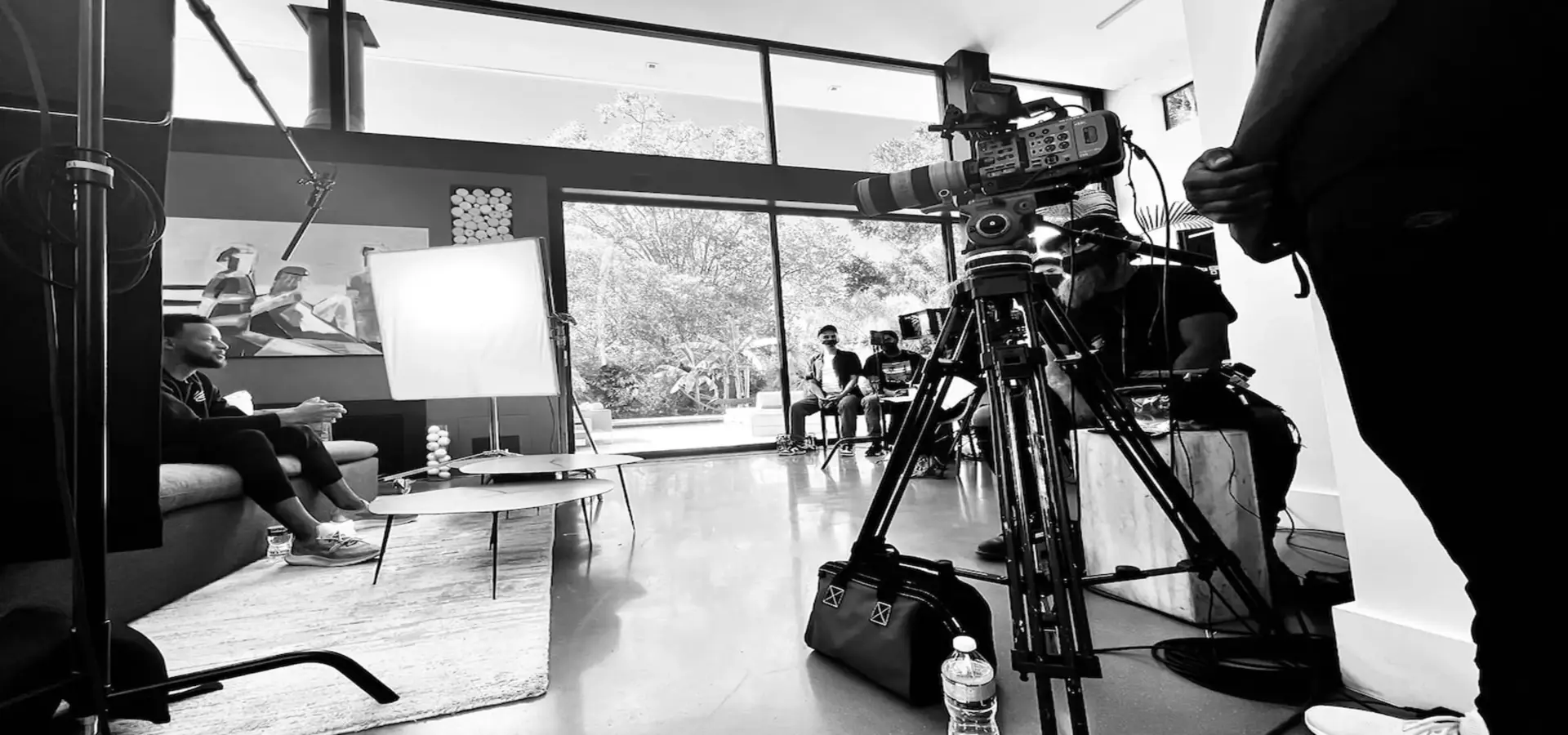 cis-services-page-documentary-film-production5-blackpopbts-steph-curry Black and white of Steph Curry on set sitting on a couch with tables near him along with crew and equipment