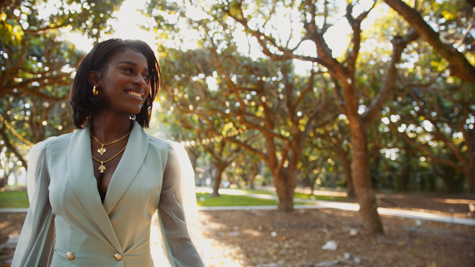 IU African American woman wearing a white dress coat looking off to the side smiling in a park