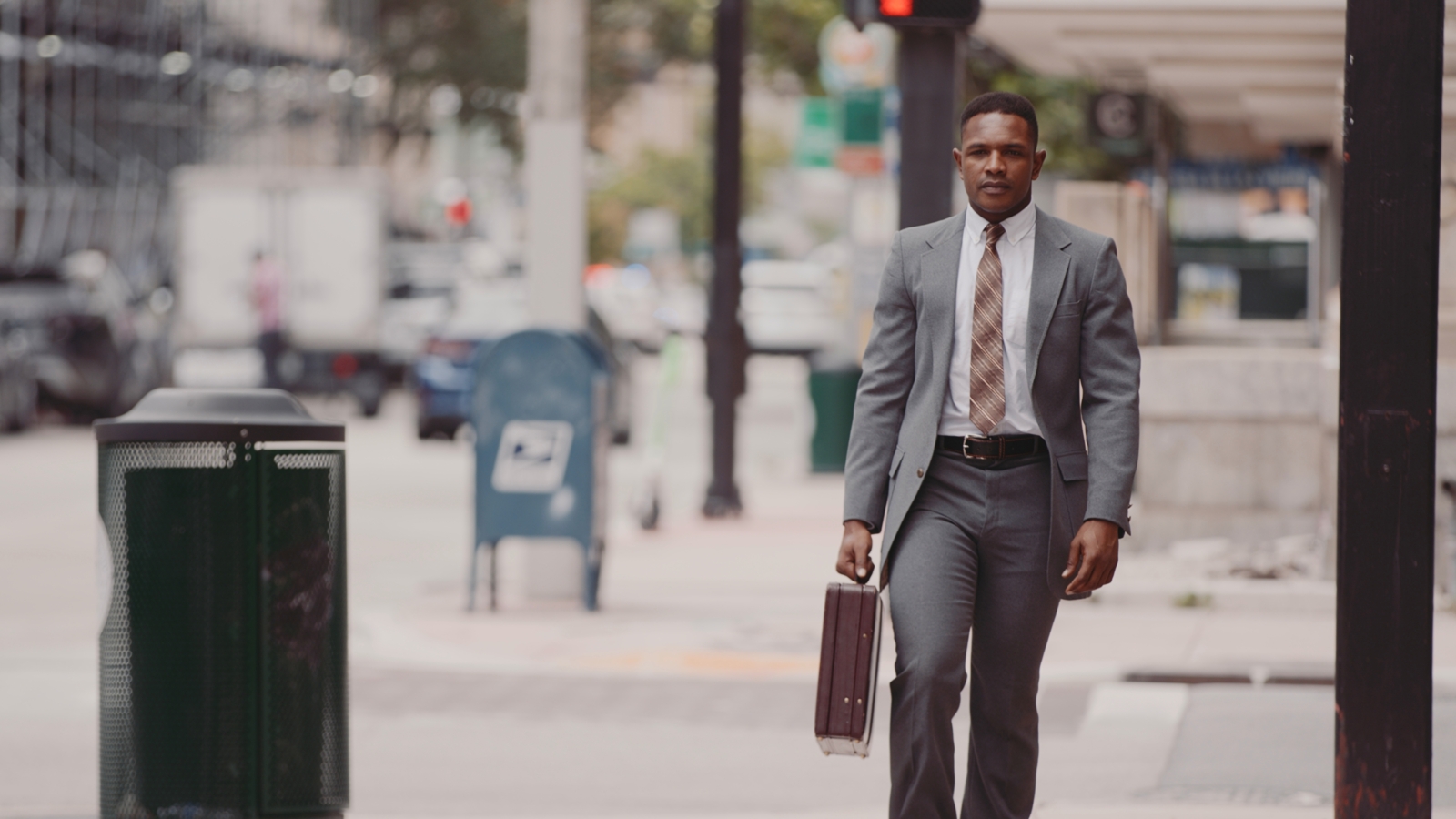 IU African American man walking down a city street wearing a gray suit carrying a brown briefcase