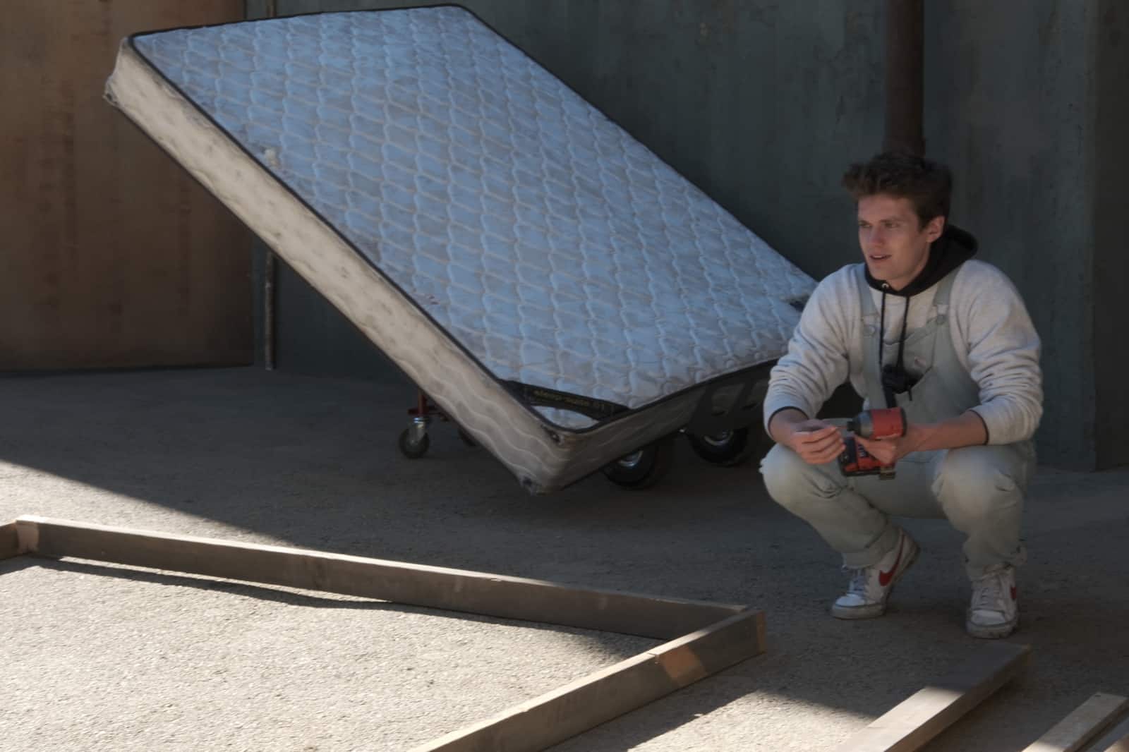 Assistant crouching on set wearing overalls holding a drill