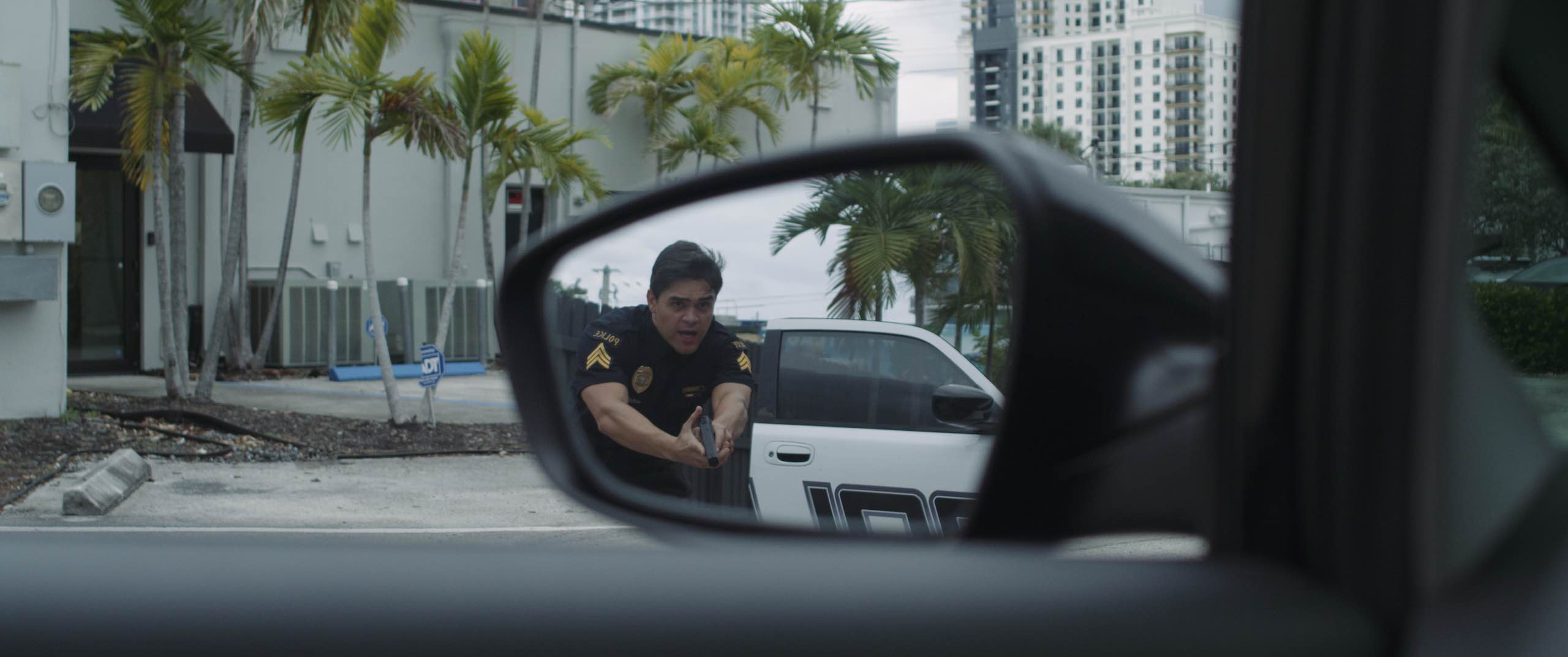 View of cop in a car side mirror with gun drawn
